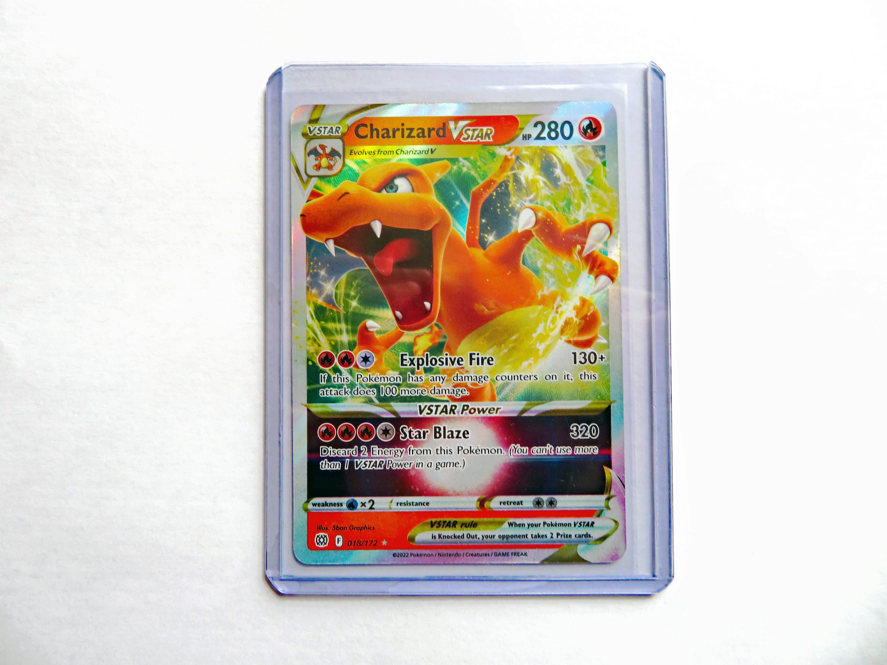 Carte Pokémon Charizard VSTAR rare imprimée, holographique, dans pochette transparente avec énergie feu et attaques Explosive Fire et Star Blaze.